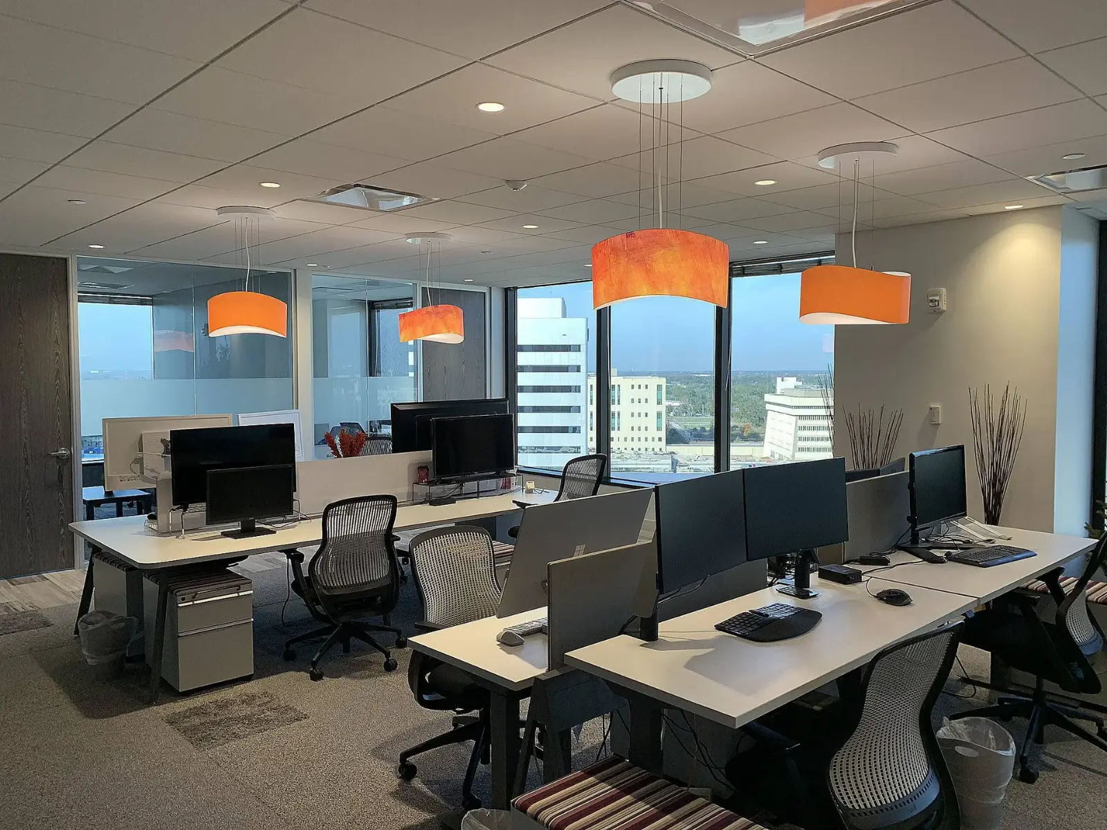 Open workstations with orange pendant lights and city windows in the Orlando office